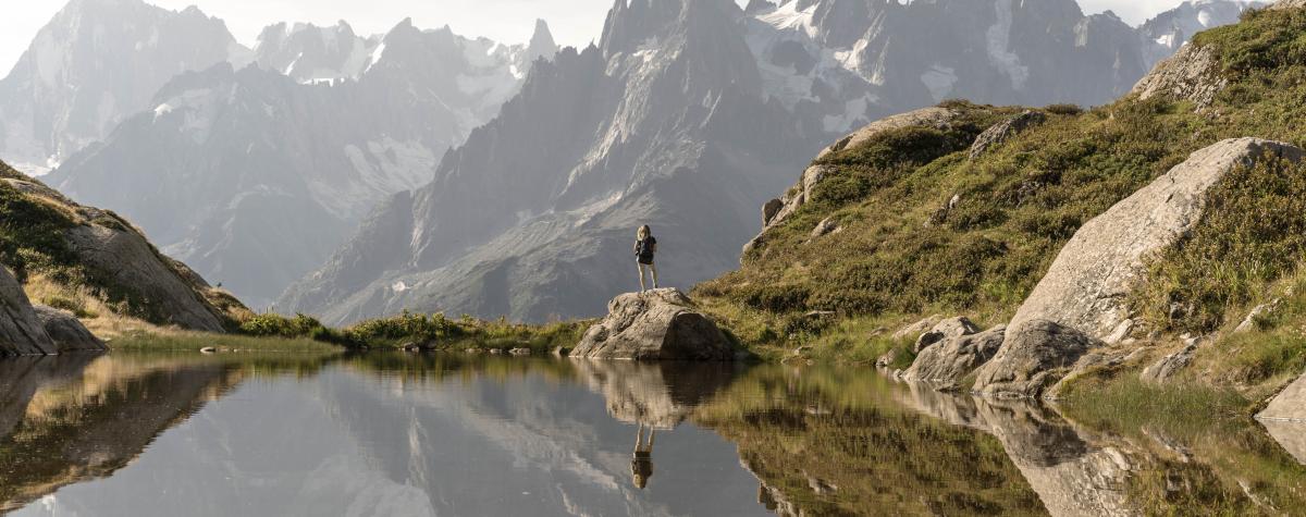A person standing with their back to a lake looking out over the mountains