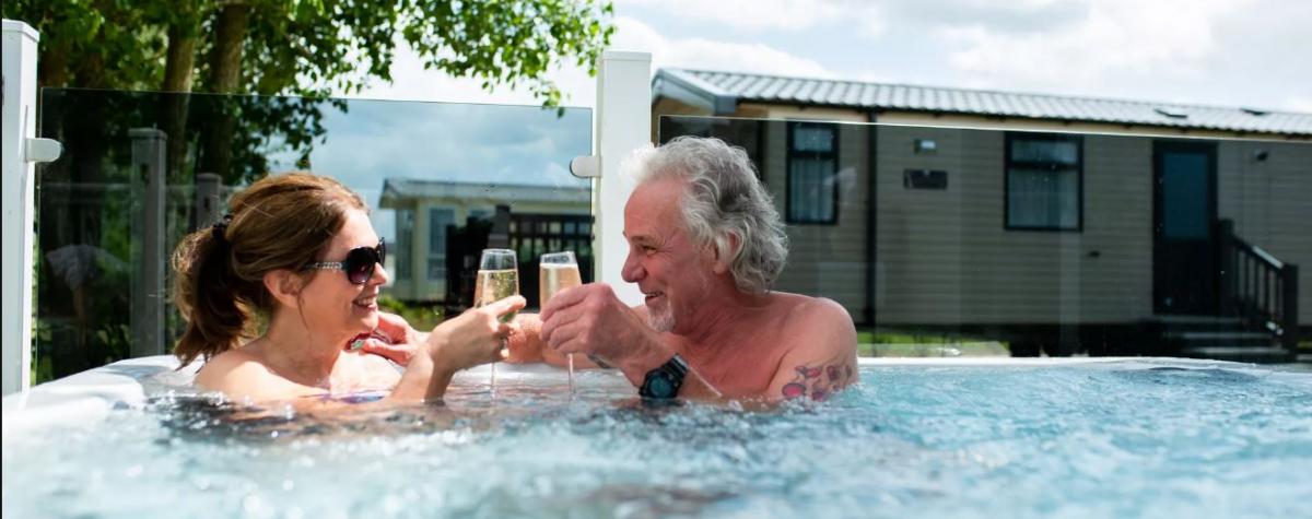 A couple in the outdoor jacuzzi close to their holiday home drinking champagne