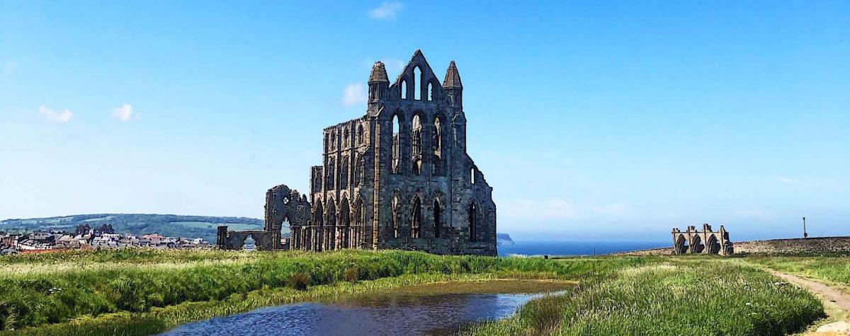An image of Whitby Cathederal with the town and sea in the distance on a warm sunny day