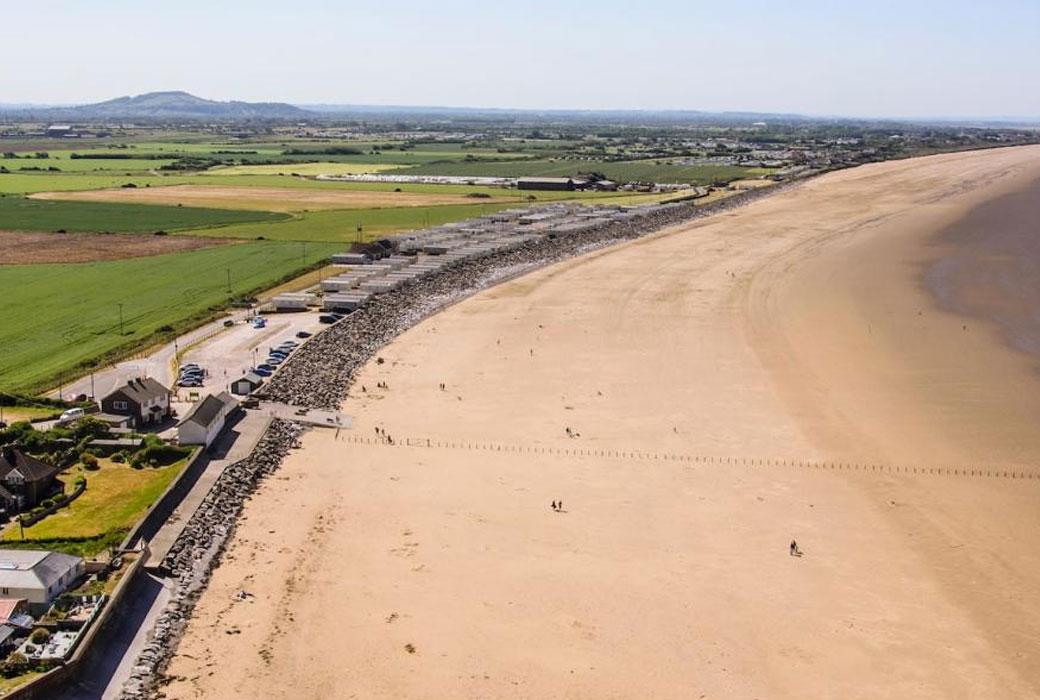 Long Golden Sand Coloured Beach with Green hills in the Background