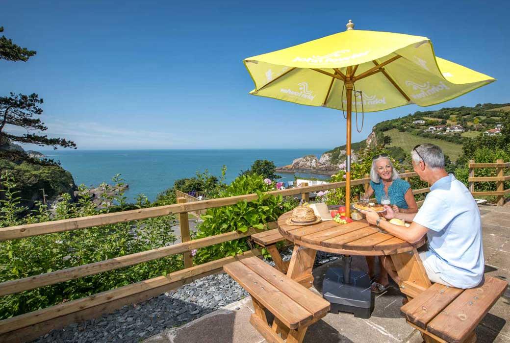 Two people sat at a table with refreshments overlooking the sea at Combe Martin